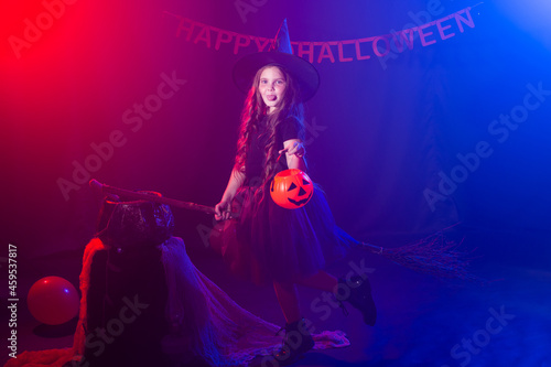 Little girl with funny tricky face pretend like flying on the broom on Halloween holiday. Kid girl wear witch costume. Fantasy  fairy tale and masquerade concept.