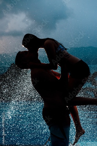 silueta de dos personas disfrutando del agua mientras llueve y se besan