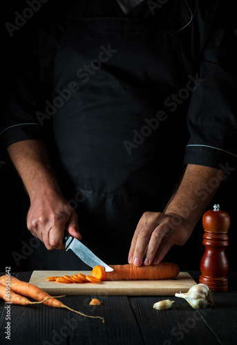 Professional chef is cutting carrots for vegetable soup in the restaurant kitchen. Close-up of the hands of the cook during work. Carrot diet