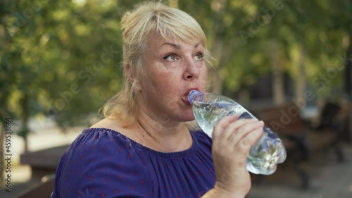 Fat woman drinking water at the street