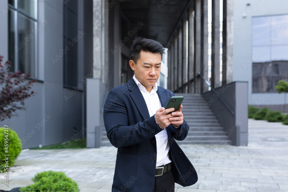 Portrait of Asian cheerful and successful businessman near office in business suit got good news read good news online Portrait of Asian cheerful and successful businessman near office in business suit got good news read good news online