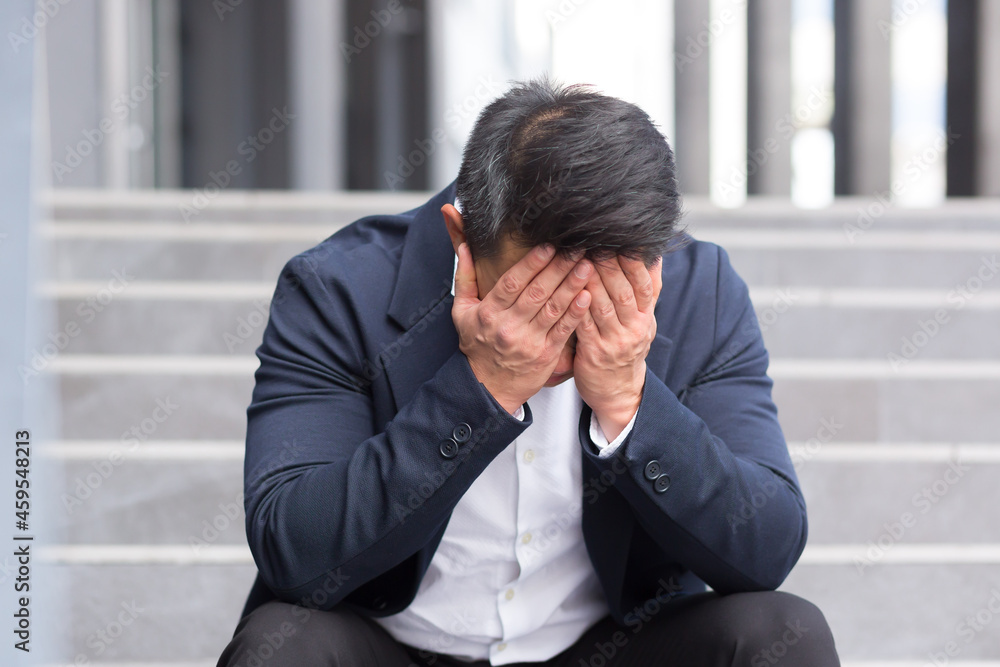 Asian businessman has a severe headache sitting on the stairs near the office Asian businessman has a severe headache sitting on the stairs near the office