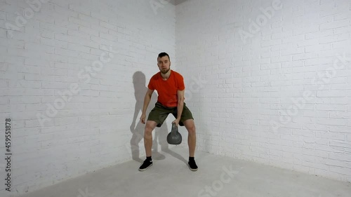 A young man in a bright T-shirt does kettlebell swings. Fitness concept. Workout.