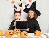 Mother and son in Halloween costumes hold an empty black frame. Copy spase. Halloween celebration concept