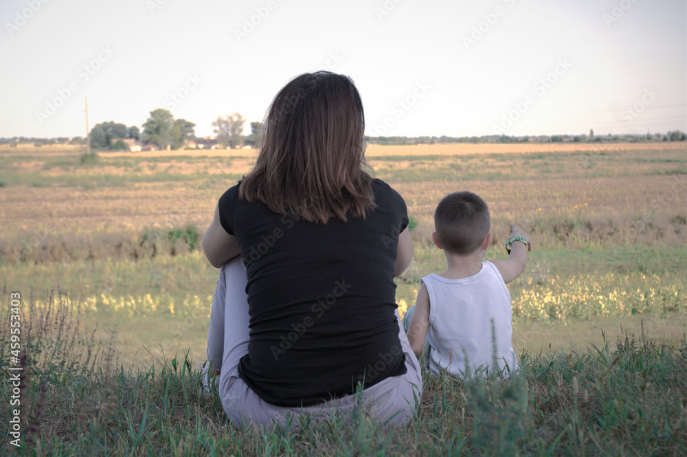 Mother and child sit the grass, and looking into the distance.