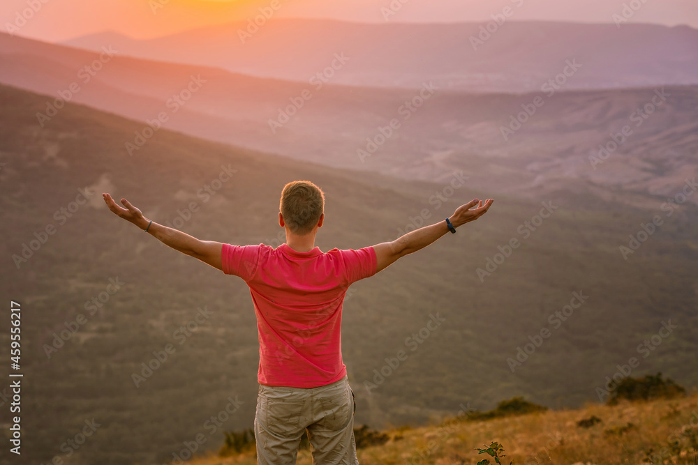 Rear view a young blond man has conquered the top of the mountain at sunset and is standing with his hands raised. Beautiful mountain landscape with a gradient. Rear view a young blond man has conquered the top of the mountain at sunset and is standing with his hands raised. Beautiful mountain landscape with a gradient.