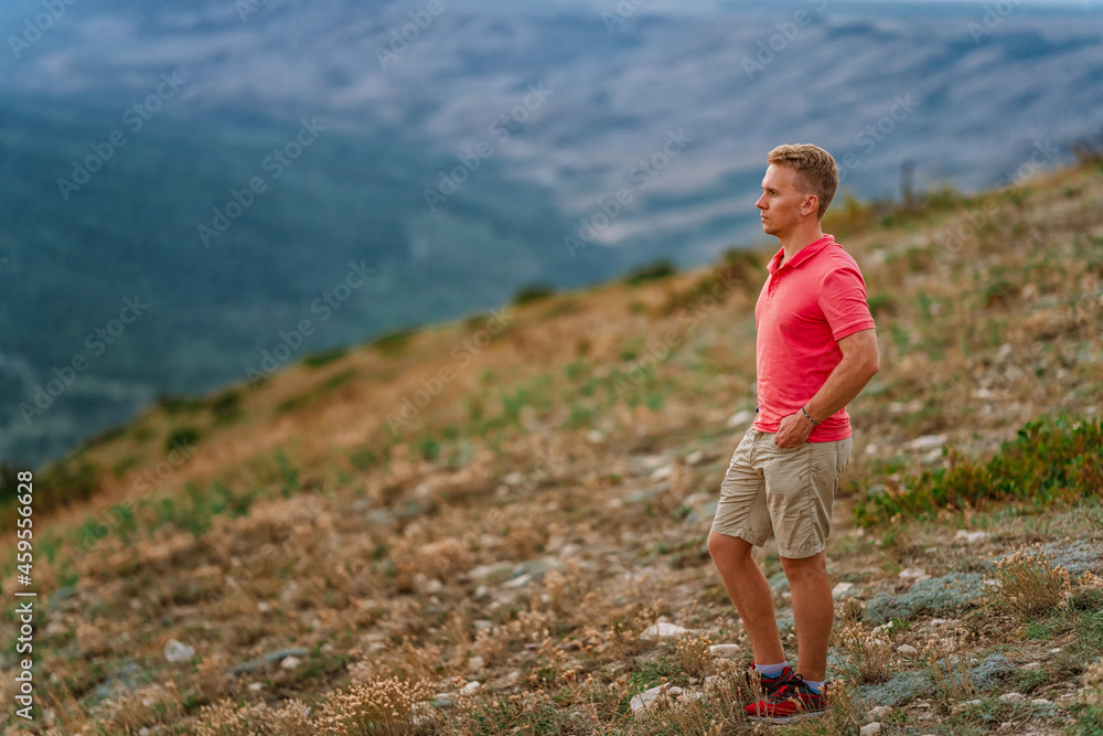 A young blond man in a pink shirt conquered the top of the mountain at sunset. Beautiful mountain landscape with a gradient. The concept of enjoying nature. A young blond man in a pink shirt conquered the top of the mountain at sunset. Beautiful mountain landscape with a gradient. The concept of enjoying nature.