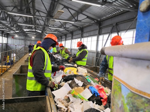 male migrant workers in green vests and orange helmets are sorting household garbage on the automatic tape of the garbage landfill