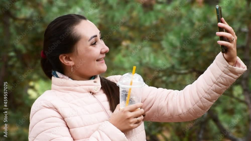 Pretty Girl makes selfie or speaking with video on telephone in the park. Autumn background. Pretty Girl makes selfie or speaking with video on telephone in the park. Autumn background.
