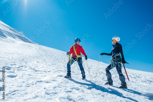 Two laughing to each other young women Rope team ascending Mont blanc du Tacul summit 4248m dressed mountaineering clothes with ice axes on snowy slopes. People extreme activities sporty concept image