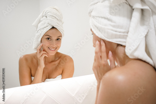 young white woman in the bathroom mirror looking at skin looking for spots signs of age and lines serious and confident in the bathroom after shower self care skin care anti aging smiling at camera