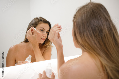 young white woman in the bathroom mirror applying serum anti acne anti aging spots signs of age and lines confident in the bathroom after shower self care skin care anti aging young adult cosmetics