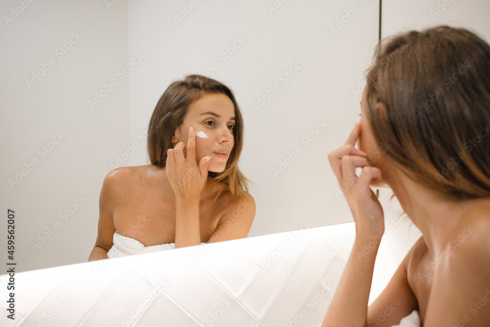 young white woman in the bathroom mirror applying face cream anti acne anti aging spots signs of age confident in the bathroom after shower self care skin care young adult cosmetics plump toned skin young white woman in the bathroom mirror applying face cream anti acne anti aging spots signs of age confident in the bathroom after shower self care skin care young adult cosmetics plump toned skin