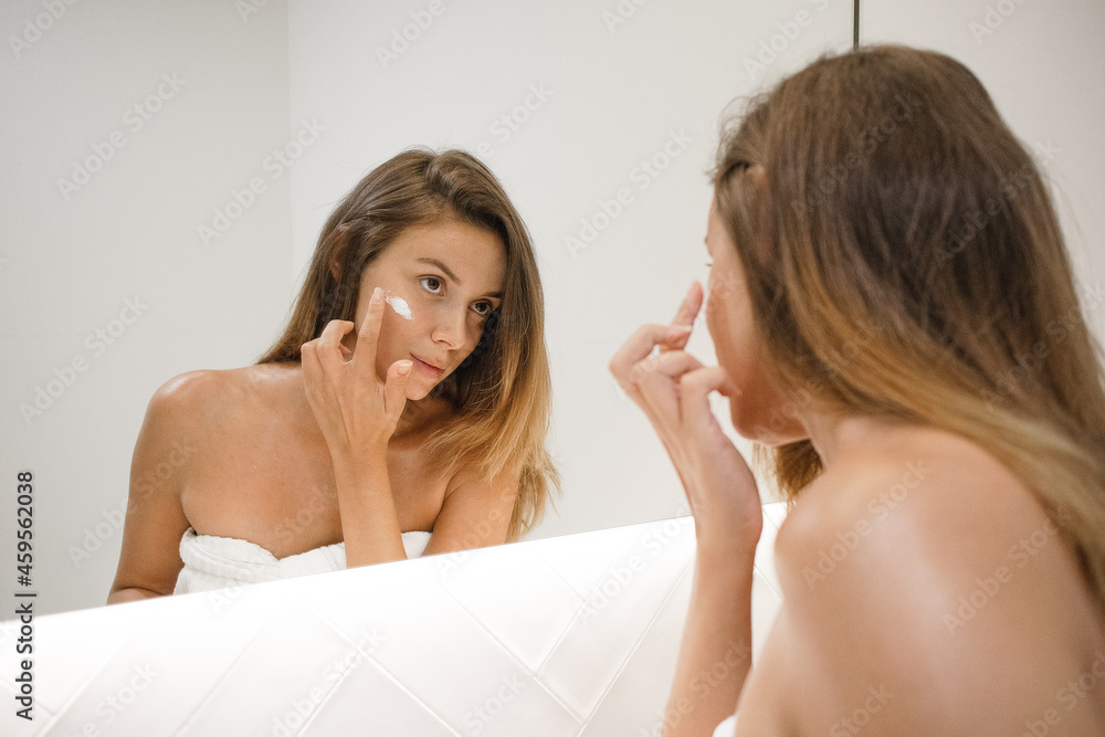 young white woman in the bathroom mirror applying face cream anti acne anti aging spots signs of age confident in the bathroom after shower self care skin care young adult cosmetics plump toned skin young white woman in the bathroom mirror applying face cream anti acne anti aging spots signs of age confident in the bathroom after shower self care skin care young adult cosmetics plump toned skin