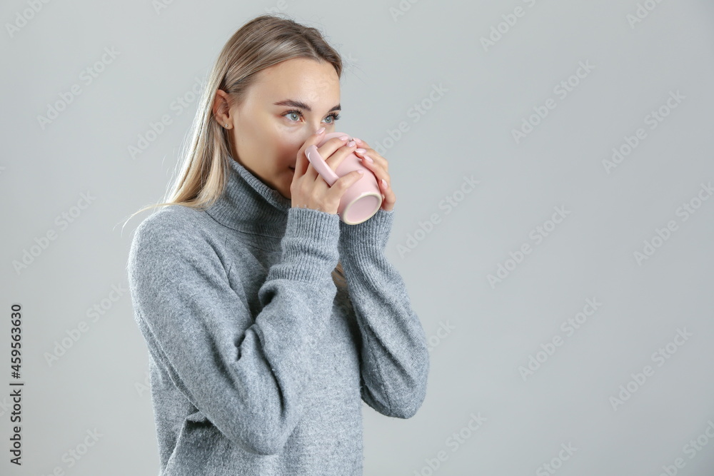 woman wearing warm sweater drinks a hot tea on grey background, studio shot. the concept of warming up with a hot drink. woman wearing warm sweater drinks a hot tea on grey background, studio shot. the concept of warming up with a hot drink.