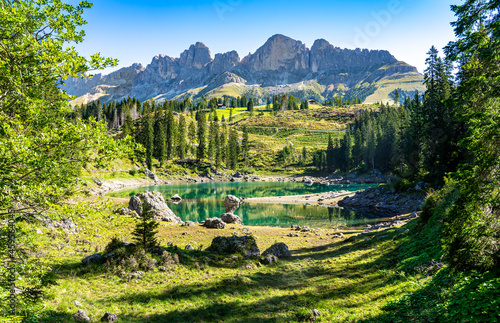 Der berühmte Karersee / Lago di Carezza in den Dolomiten, Südtirol: Panoramabild mit Blüten und Berggipfeln photo