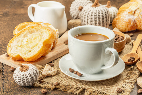 Breakfast concept with a cup of coffee, croissants, milk jug, and decorative crochet pumpkins