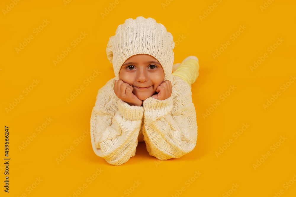 a boy in a white winter hat in a knitted white sweater and socks on a yellow background