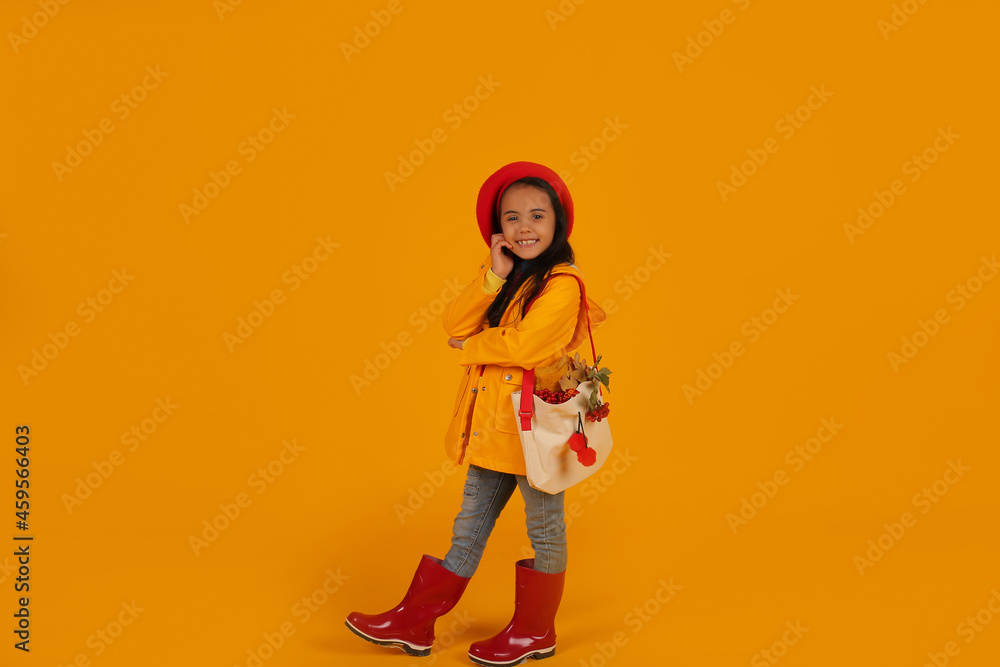 a girl in a red beret with pink glasses in a yellow raincoat and red boots has a bag with autumn flowers on her shoulder