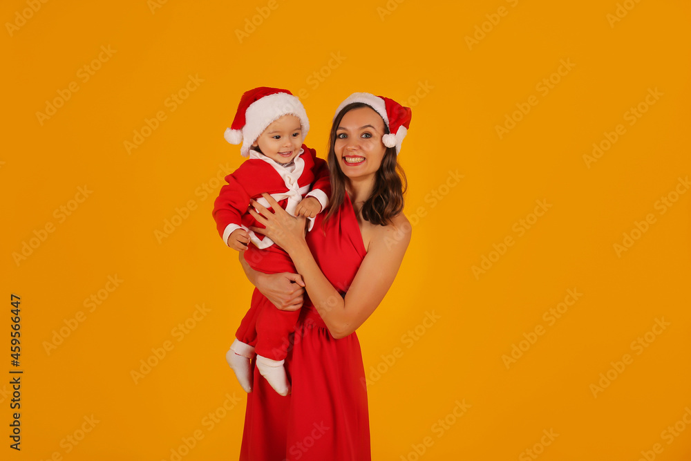 a beautiful young girl in a red dress holds her son in a Santa Claus costume and a Santa Claus hat for the new year a beautiful young girl in a red dress holds her son in a Santa Claus costume and a Santa Claus hat for the new year