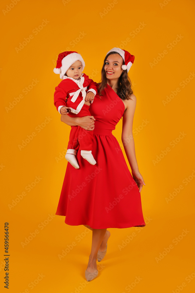 a beautiful young girl in a red dress holds her son in a Santa Claus costume and a Santa Claus hat for the new year