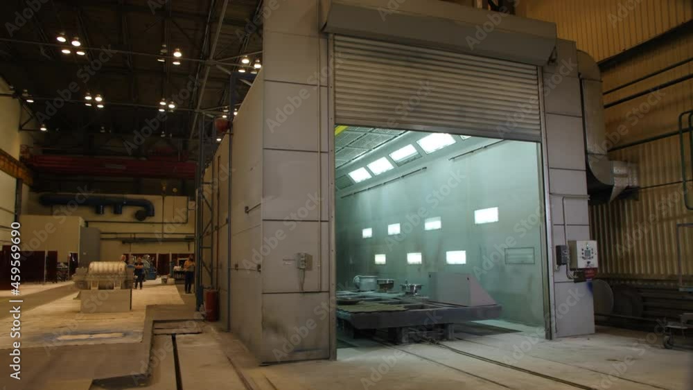 Male worker paints large metal details with spray gun in brightly lit coating room in production plant workshop Male worker paints large metal details with spray gun in brightly lit coating room in production plant workshop