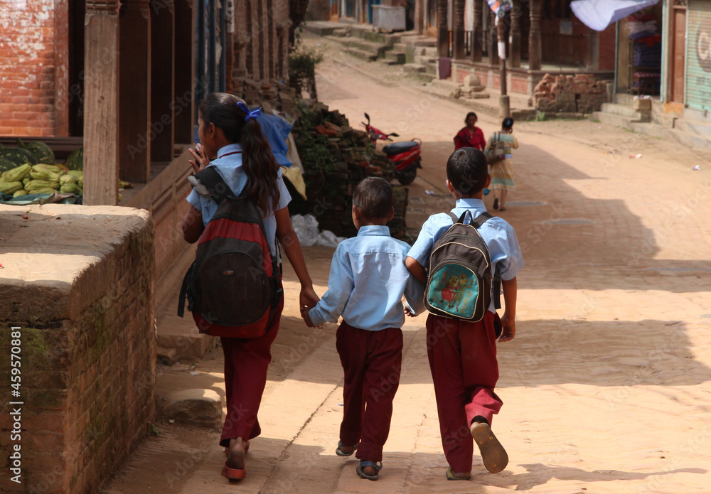 Nepalese grade-schoolers wearing uniforms walking hand in hand in the street.