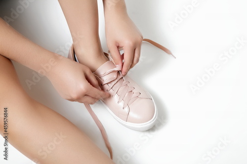 female hands tying pink sneaker on white background.