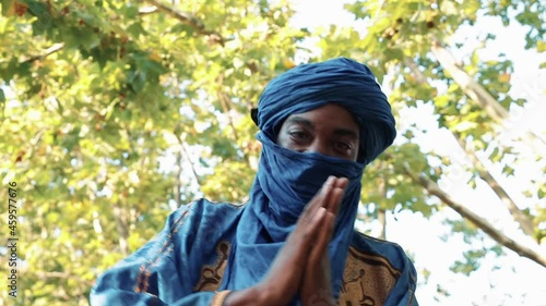 Man in traditional blue Tuareg dresses, danced in a park. Blurred background of trees.