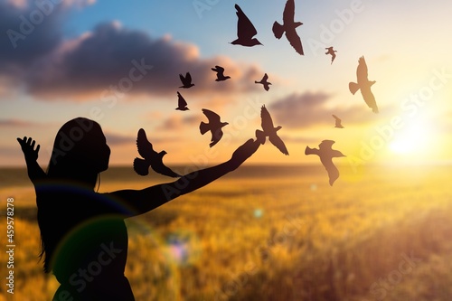 Hope faith concept. Woman launches birds on the background of a sunny sunset.
