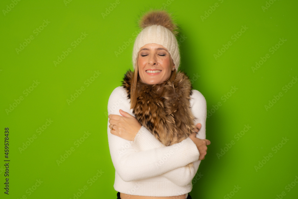 Portrait of a pretty young woman in winter clothes hugging herself standing isolated over green background Portrait of a pretty young woman in winter clothes hugging herself standing isolated over green background