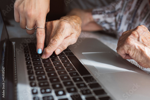 Young granddaughter teaching laptop to grandmother at home