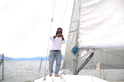 Latino adult man drives a sailboat on the lake with sails unfurled as a physical activity, sport and hobby to relax for the weekend 