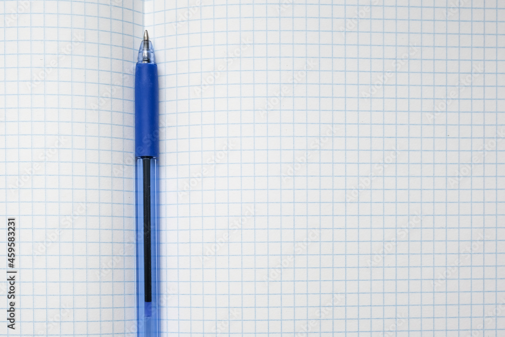 A blue ball pen lying on a blank checkered school notebook sheet , paper with copy space A blue ball pen lying on a blank checkered school notebook sheet , paper with copy space