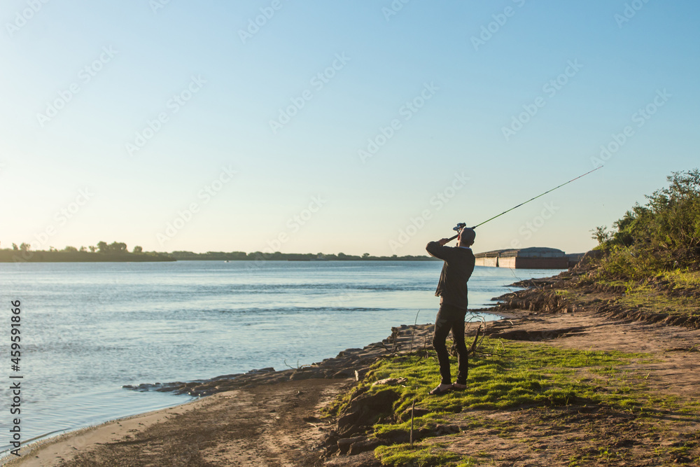 Young man prepared to cast his fishing rod into the water at the river's edge. Young man prepared to cast his fishing rod into the water at the river's edge.
