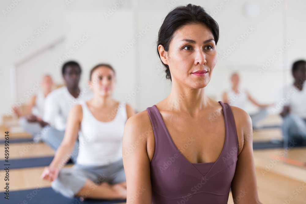 Closeup portrait of attractive positive asian woman meditating in Padmasana posture during group training in yoga studio