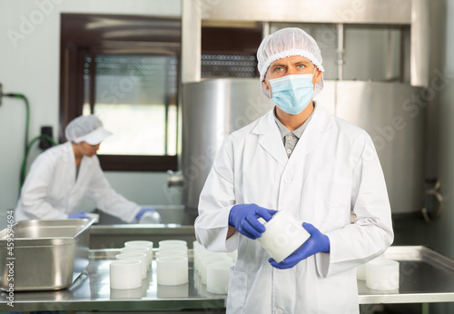 Worker in white coat and in protective mask working at cottage cheese production on dairy factory