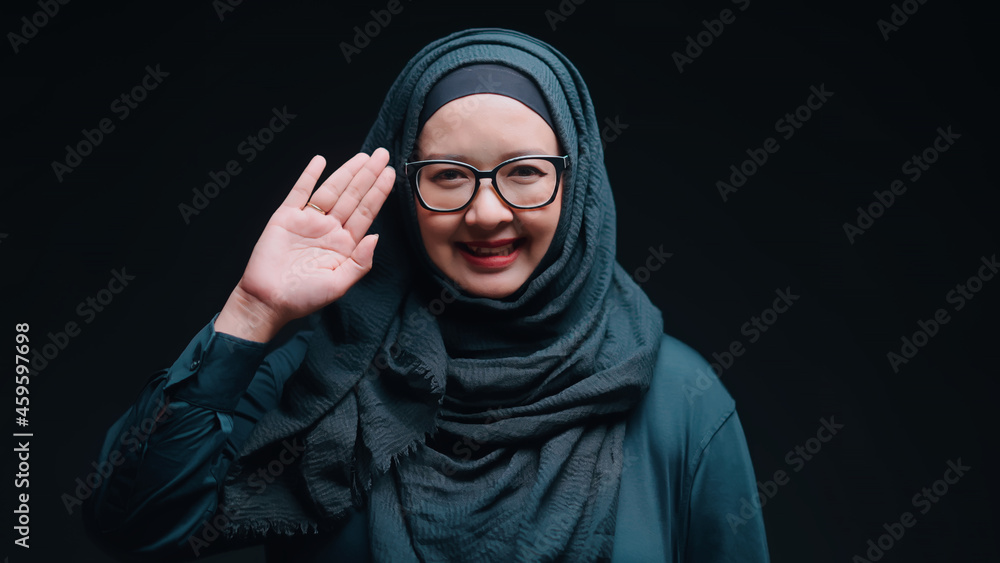 A beautiful middle-aged Asian Muslim woman. Standing smiling and raising a salam hand to greet the camera with bright cuteness A beautiful middle-aged Asian Muslim woman. Standing smiling and raising a salam hand to greet the camera with bright cuteness