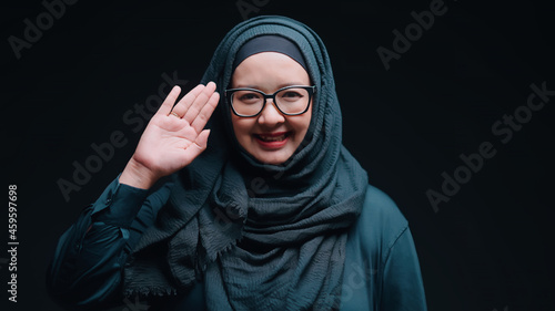 A beautiful middle-aged Asian Muslim woman. Standing smiling and raising a salam hand to greet the camera with bright cuteness