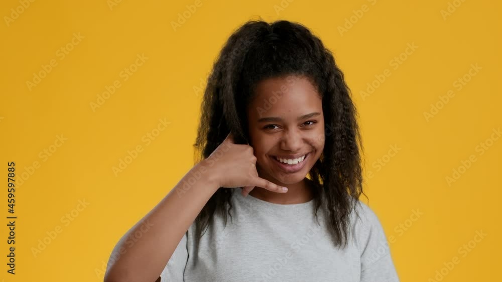 Funny African Teenager Girl Showing Call Me Gesture, Yellow Background Funny African Teenager Girl Showing Call Me Gesture, Yellow Background