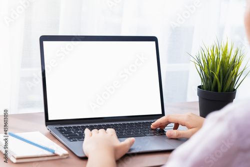 Woman using and typing on Laptop with a mockup white screen on wooden table.