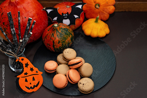 Dessert for Halloween. Thanksgiving menu. French macarons. Macaroons with chocolate on a black background with pumpkins and eco cocktail straws. Soft selective focus. Copy space