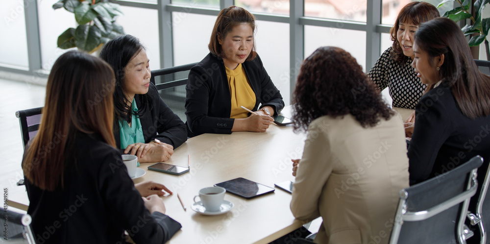 Fototapeta premium Group of businesswomen in formal business clothing sitting together around meeting table taking note in conference room brainstorming discussing planning about working marketing strategy in company