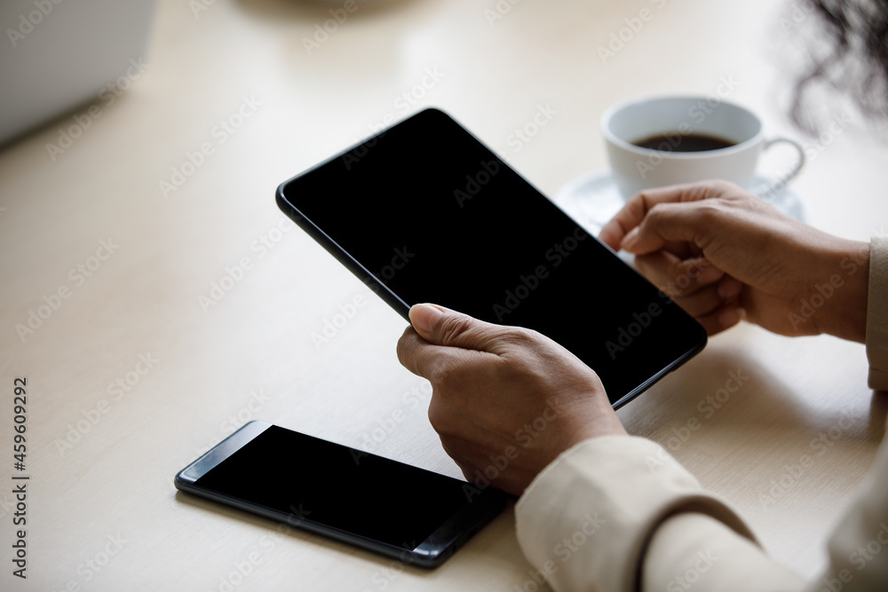 Close up shot of blank black screen touchscreen tablet computer holding in hands of unrecognizable unidentified businesswoman for advertising text and copy space near smartphone and hot coffee cup Close up shot of blank black screen touchscreen tablet computer holding in hands of unrecognizable unidentified businesswoman for advertising text and copy space near smartphone and hot coffee cup