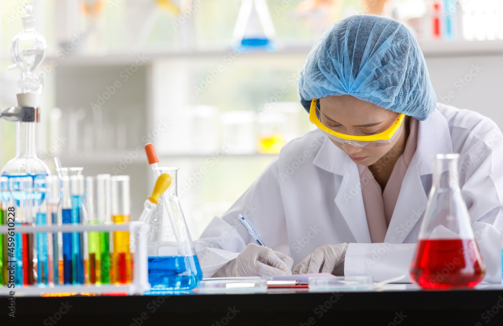Asian female scientist in white lab coat safety goggles hygiene cap and rubber gloves writing result note on board when do science experiment on laboratory working desk with glass test tube beakers Asian female scientist in white lab coat safety goggles hygiene cap and rubber gloves writing result note on board when do science experiment on laboratory working desk with glass test tube beakers