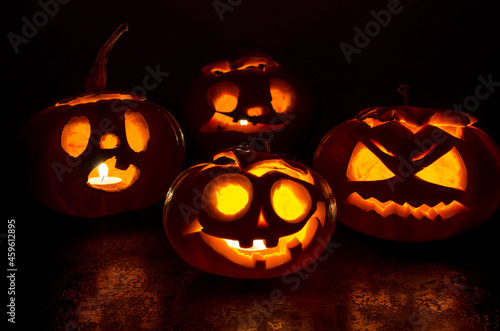Halloween carved bright orange pumpkin jack lantern with different expressions of immotions on a dark textured background glow brightly in the dark