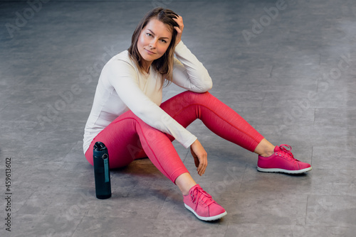 Middle age tired and relaxed woman in sportswear posing in modern gym