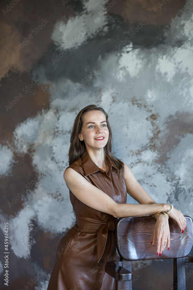 Portrait of a beautiful young business woman with brown hair in a brown dress. Side view of happy smiling girl with red lips on gray background with copy space. The concept of business and success.