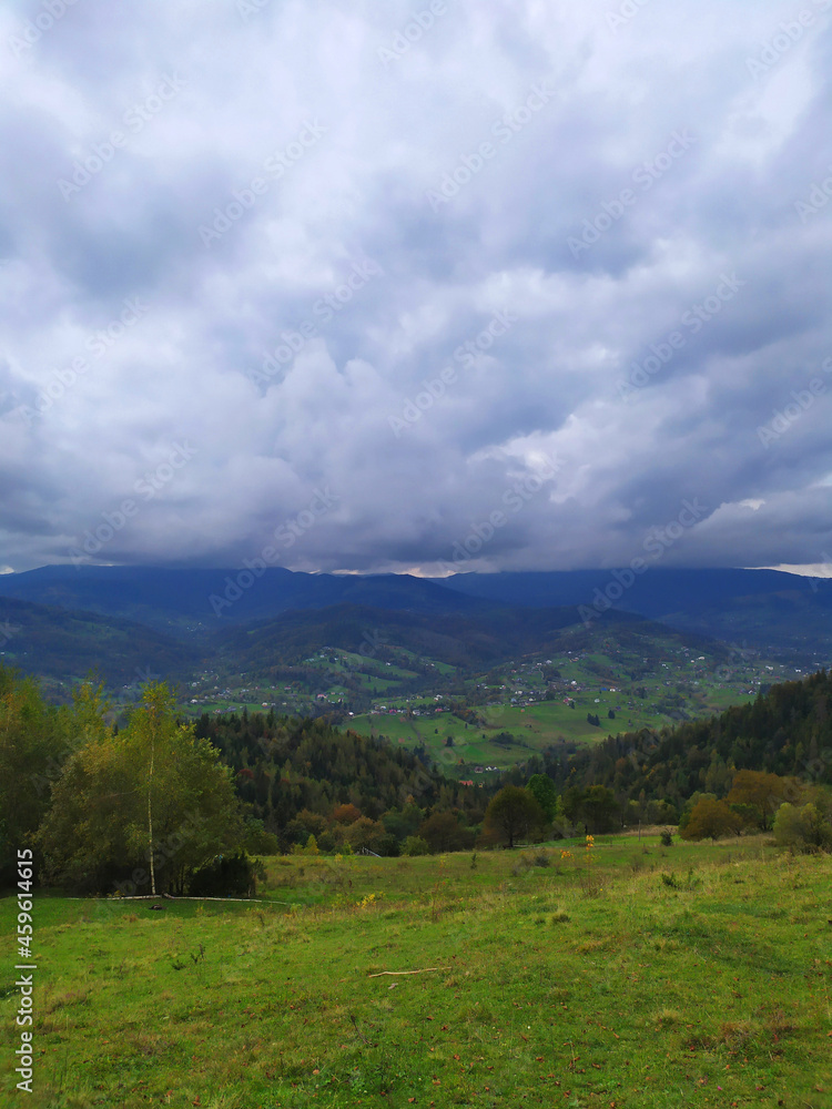 Carpathian landscape with cloudy sky. A green meadow in mountains near old forest. Lifestyle in the Carpathian village. Ecology protection concept. Explore the beauty of the world.