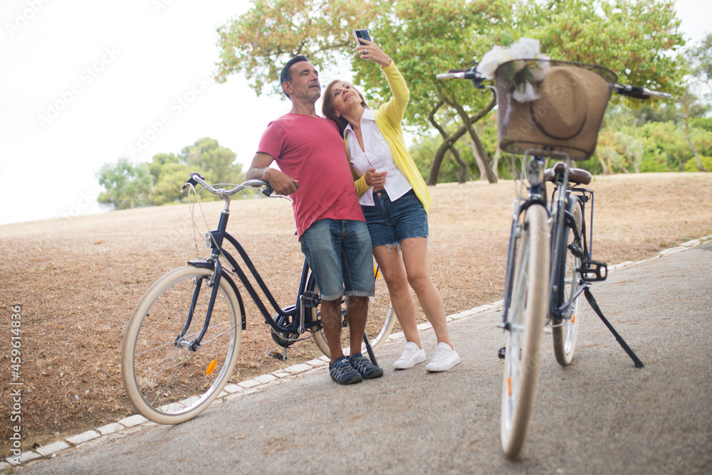 Obraz premium Happy mature couple taking selfie with bikes in park. Senior man and woman dating in fall. Active seniors, mature love concept